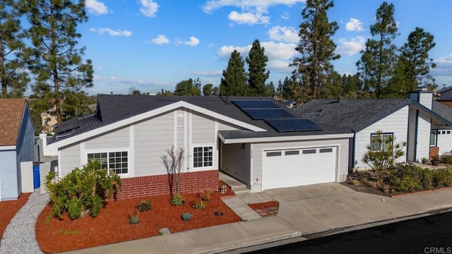 single story home with a garage, a shingled roof, solar panels, concrete driveway, and brick siding