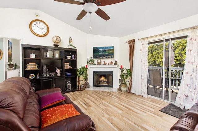 living area featuring a ceiling fan, vaulted ceiling, a tiled fireplace, and wood finished floors