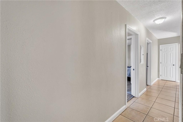 hall with light tile patterned floors, baseboards, and a textured ceiling