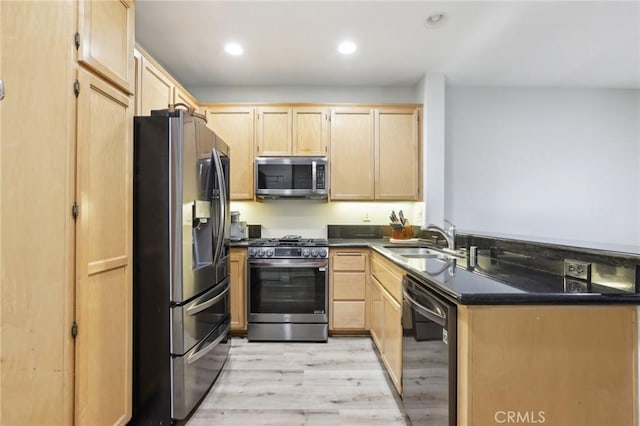 kitchen with dark countertops, light brown cabinetry, appliances with stainless steel finishes, light wood-style floors, and a sink