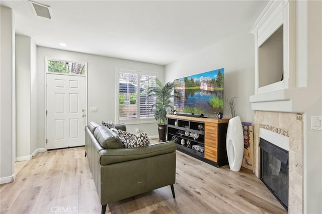 living area with visible vents, a tiled fireplace, light wood-style flooring, and baseboards