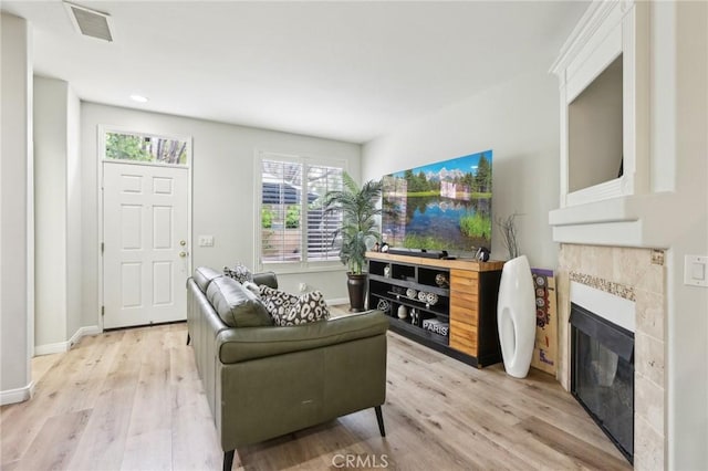 living area featuring a tiled fireplace, visible vents, light wood-style flooring, and baseboards