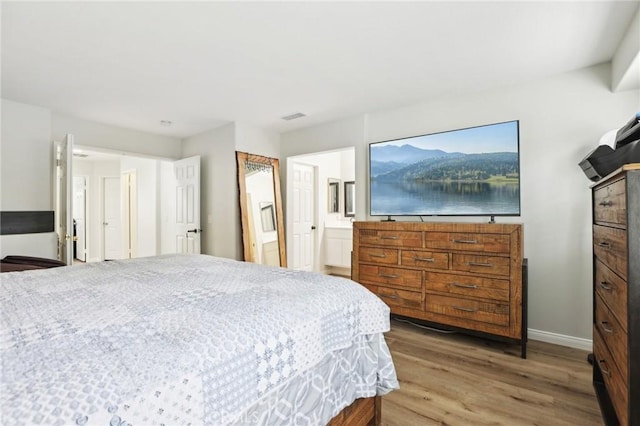 bedroom featuring visible vents, ensuite bath, baseboards, and wood finished floors