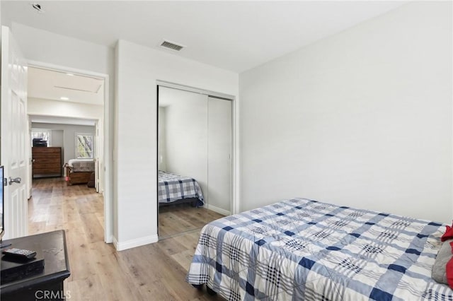 bedroom with a closet, visible vents, light wood-style flooring, attic access, and baseboards