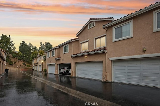 view of front facade with a tiled roof, aphalt driveway, an attached garage, and stucco siding