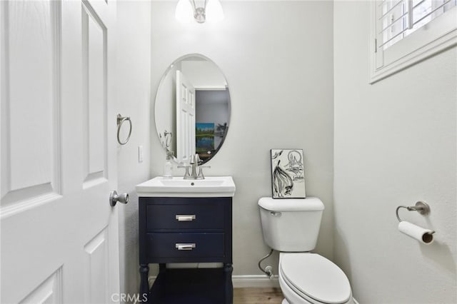 half bathroom with wood finished floors, vanity, toilet, and baseboards