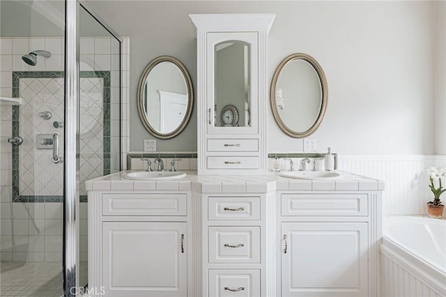 bathroom with wainscoting, a sink, a shower stall, and double vanity