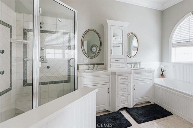 bathroom featuring a wainscoted wall, a garden tub, tile patterned flooring, a shower stall, and a sink