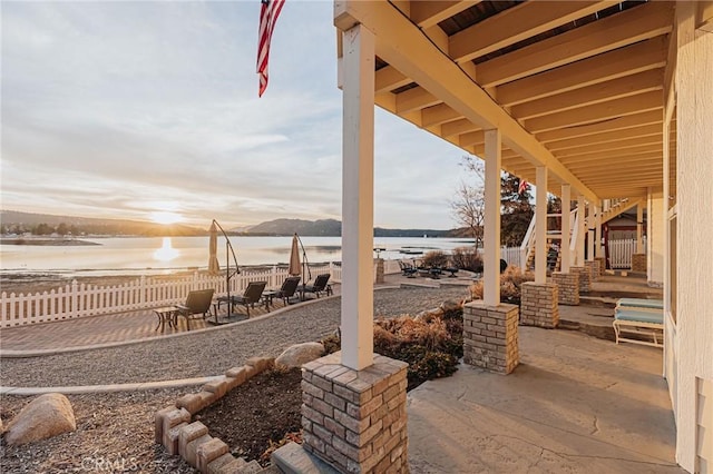 patio terrace at dusk with stairway, a water view, and fence