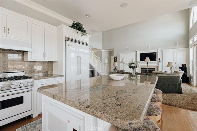 kitchen featuring white cabinets, custom range hood, open floor plan, built in refrigerator, and white gas stove