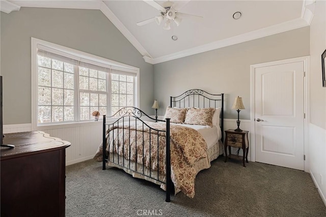 bedroom with a wainscoted wall, vaulted ceiling, dark carpet, and a ceiling fan