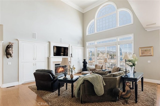 living room with light wood finished floors, a high ceiling, ornamental molding, a glass covered fireplace, and baseboards