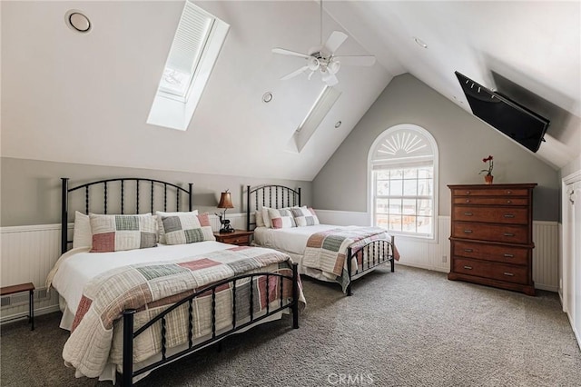 bedroom featuring ceiling fan, dark carpet, vaulted ceiling with skylight, and wainscoting