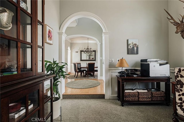 interior space featuring arched walkways, crown molding, a notable chandelier, dark colored carpet, and ornate columns