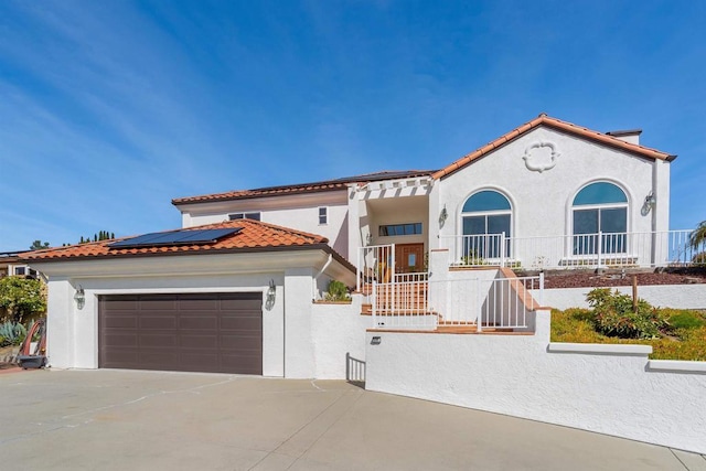 mediterranean / spanish home with a garage, driveway, a tiled roof, roof mounted solar panels, and stucco siding