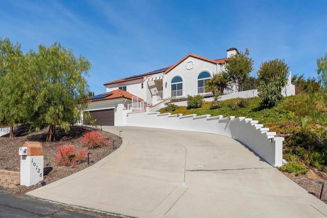 mediterranean / spanish-style house featuring a garage, concrete driveway, stucco siding, and solar panels