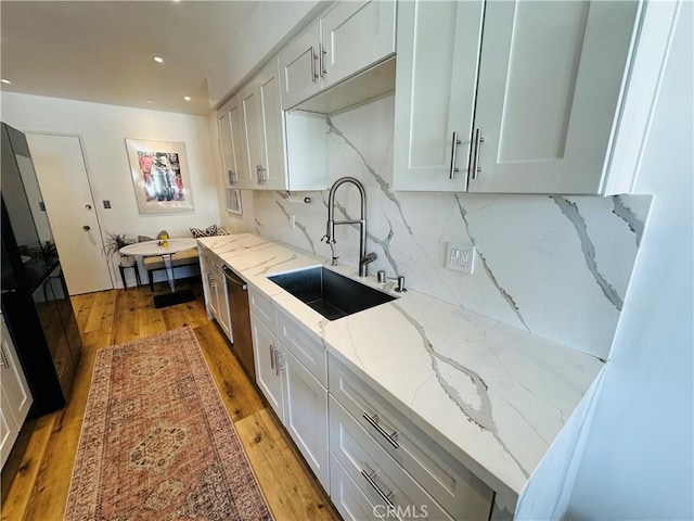 kitchen with decorative backsplash, dishwasher, light stone counters, light wood-style floors, and a sink