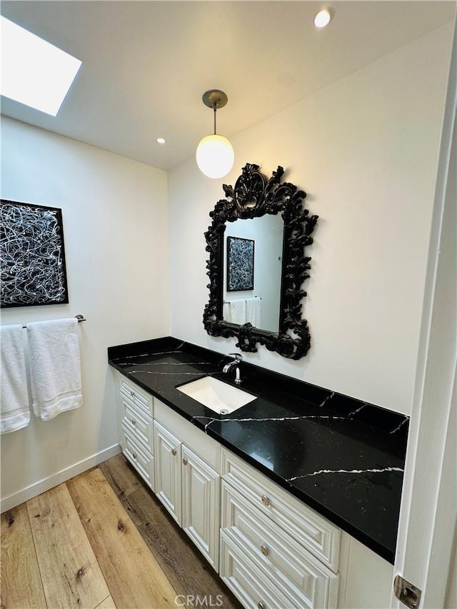 bathroom featuring a skylight, recessed lighting, vanity, wood finished floors, and baseboards