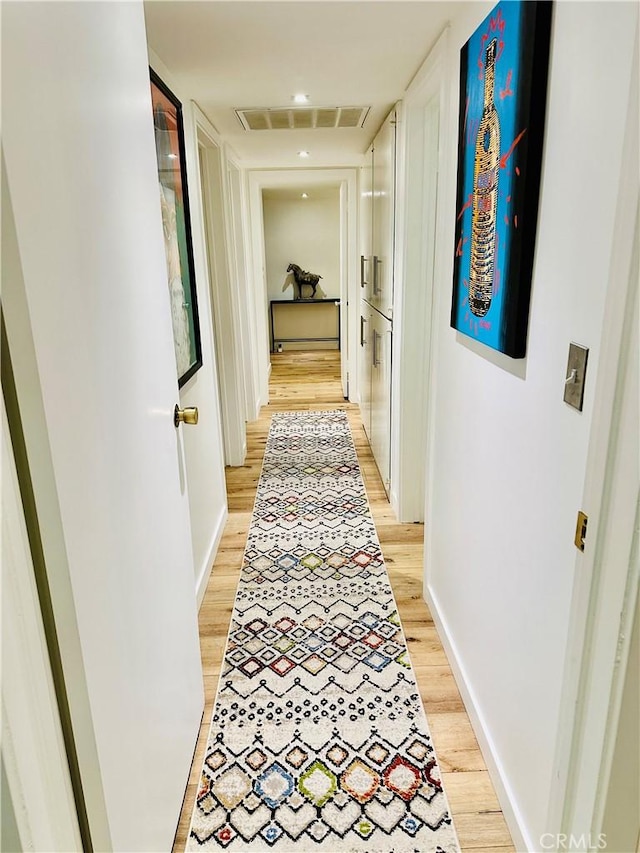 hallway with light wood finished floors, baseboards, and visible vents