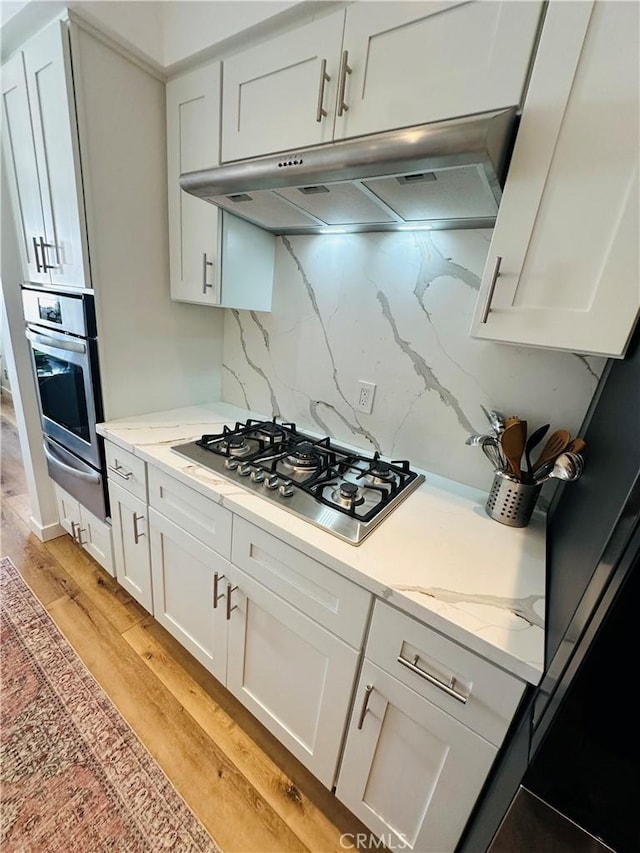 kitchen with appliances with stainless steel finishes, white cabinetry, a warming drawer, and under cabinet range hood