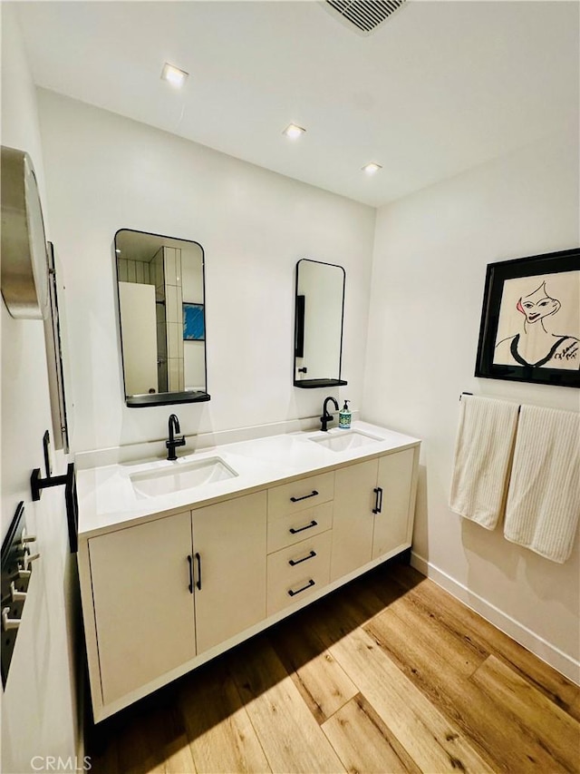 full bath featuring double vanity, wood finished floors, a sink, and baseboards