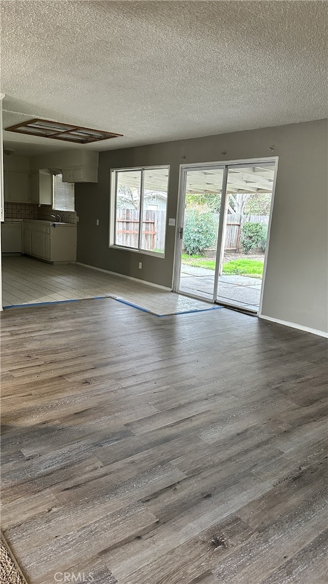 unfurnished living room with a sink, a textured ceiling, baseboards, and wood finished floors