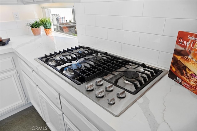 interior details featuring tasteful backsplash, white cabinets, stainless steel gas stovetop, and light stone counters