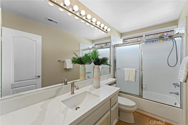 bathroom featuring visible vents, bath / shower combo with glass door, toilet, wood finished floors, and vanity