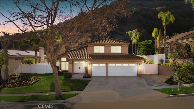 mediterranean / spanish house featuring stucco siding, concrete driveway, a front yard, fence, and a tiled roof