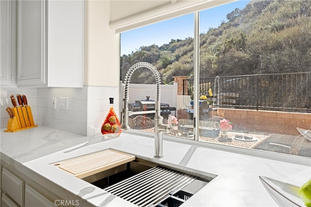 interior details with tasteful backsplash, white cabinets, a sink, and light stone counters