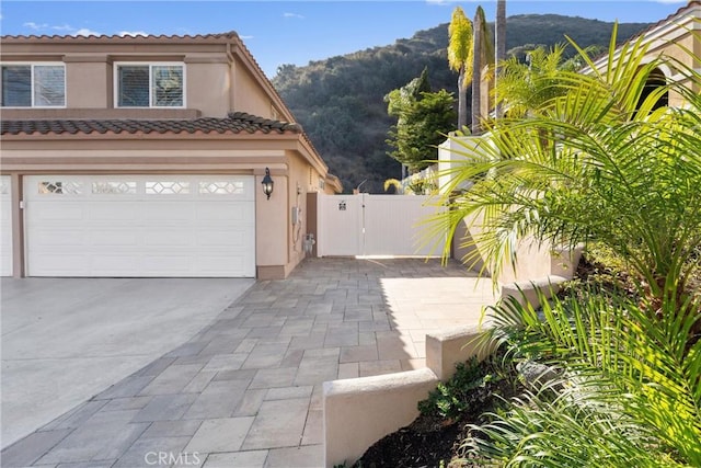 view of side of home featuring a garage, a tile roof, driveway, a gate, and stucco siding