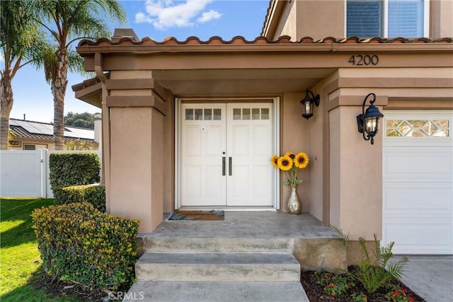 doorway to property featuring a garage, fence, and stucco siding