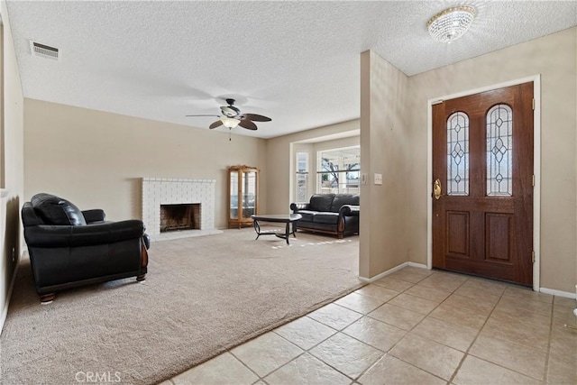 entryway featuring visible vents, light colored carpet, ceiling fan, a textured ceiling, and a brick fireplace