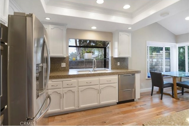 kitchen with a sink, stainless steel appliances, a raised ceiling, and white cabinetry