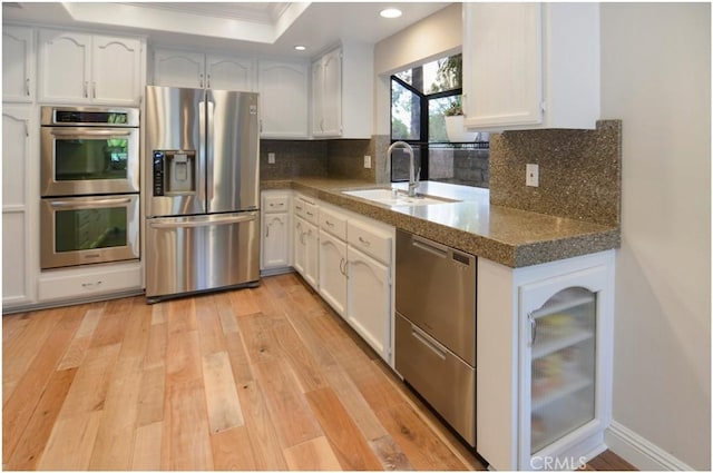 kitchen with a sink, white cabinetry, light wood-style floors, appliances with stainless steel finishes, and tasteful backsplash