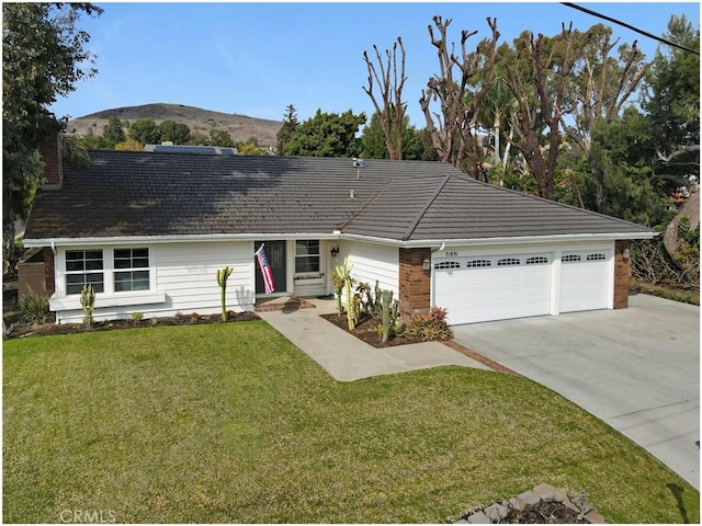 single story home with concrete driveway, an attached garage, a front yard, a mountain view, and brick siding