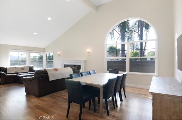 dining room with beam ceiling, high vaulted ceiling, wood finished floors, and a high end fireplace