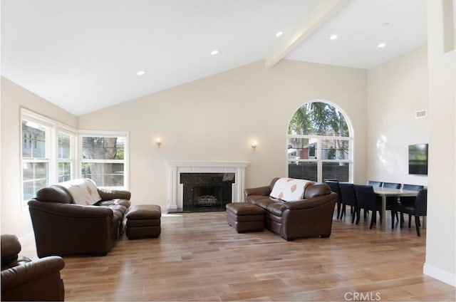 living area with high vaulted ceiling, light wood-style flooring, a fireplace, visible vents, and beam ceiling