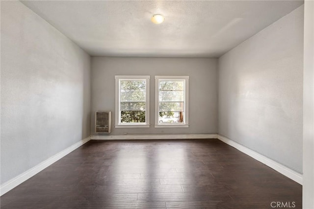 unfurnished room with heating unit, baseboards, and dark wood finished floors