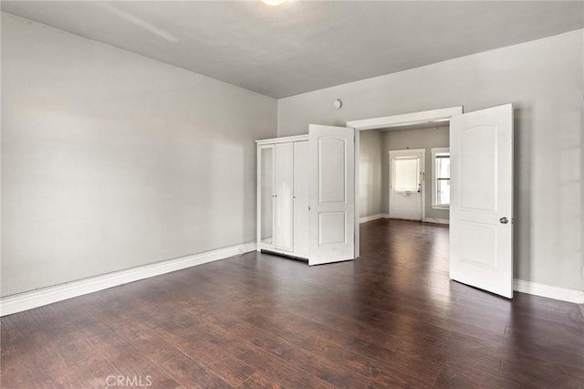 unfurnished bedroom with dark wood-type flooring, a closet, and baseboards