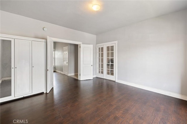 unfurnished bedroom featuring a closet, baseboards, dark wood-type flooring, and french doors