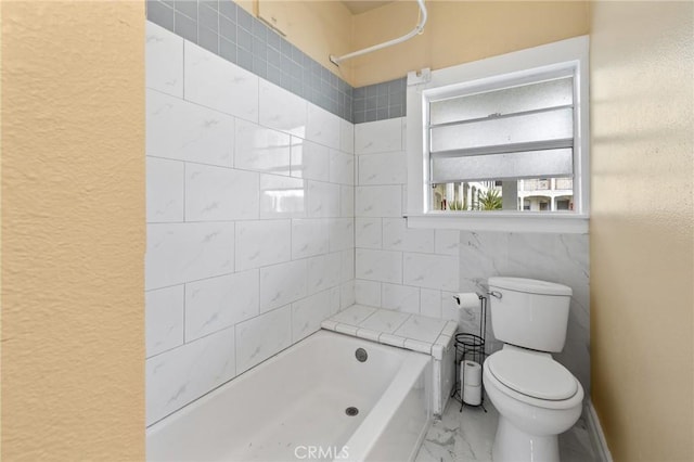 bathroom featuring a washtub, marble finish floor, a textured wall, and toilet