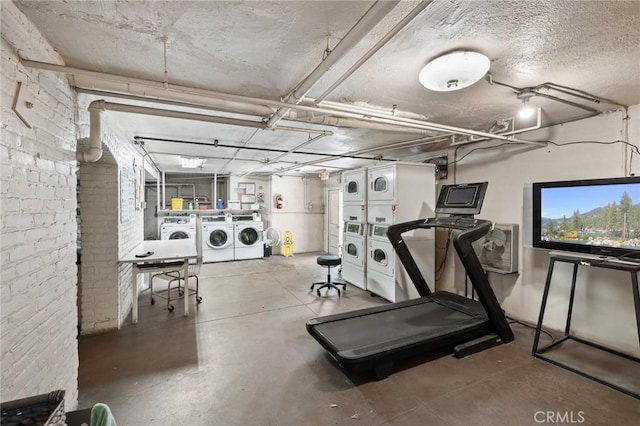 exercise room featuring a garage, brick wall, washer and clothes dryer, and stacked washer / drying machine