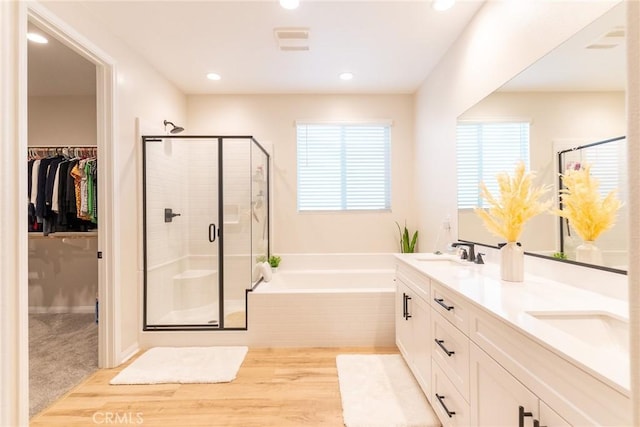 bathroom with wood finished floors, a garden tub, a spacious closet, a shower stall, and a sink