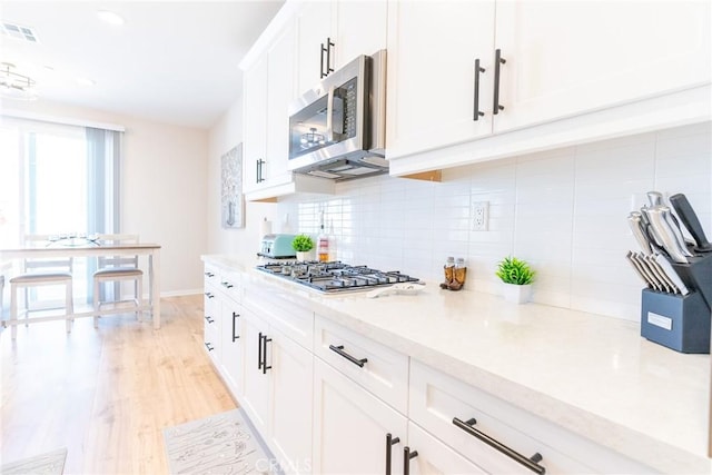 kitchen with light wood finished floors, stainless steel appliances, visible vents, decorative backsplash, and white cabinetry