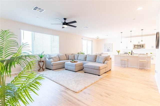 living area featuring light wood-type flooring, ceiling fan, and visible vents