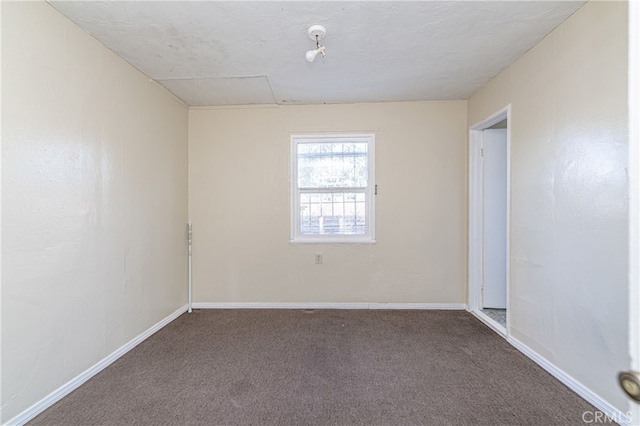 empty room featuring dark colored carpet and baseboards