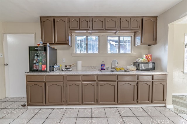 kitchen with black microwave, light countertops, a sink, and light tile patterned flooring