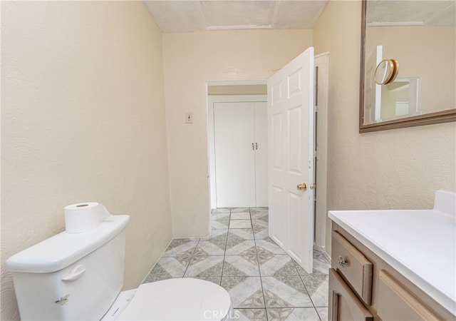 bathroom featuring a textured wall, vanity, and toilet