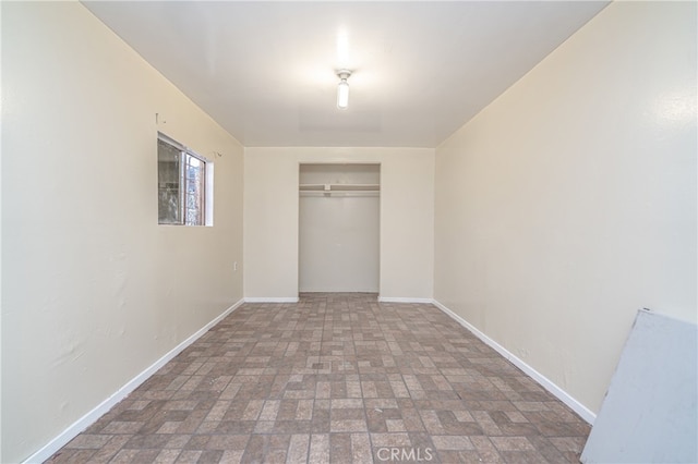 unfurnished bedroom with a closet, brick floor, and baseboards